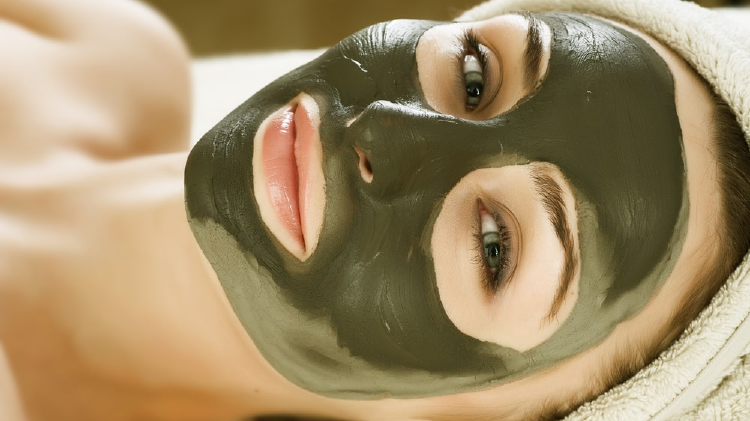 Mujer acostada con mascarilla verde en todo el rostros y toalla envolviendo su cabello