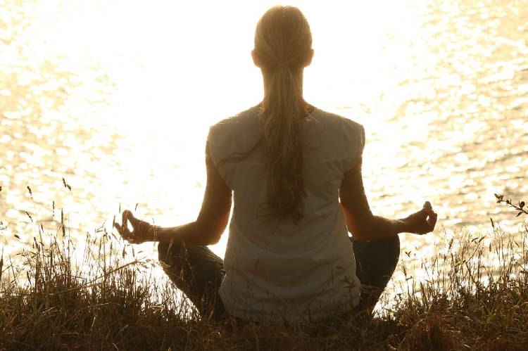 mujer meditar lago Una mujer medita frente a un lago al atardecer