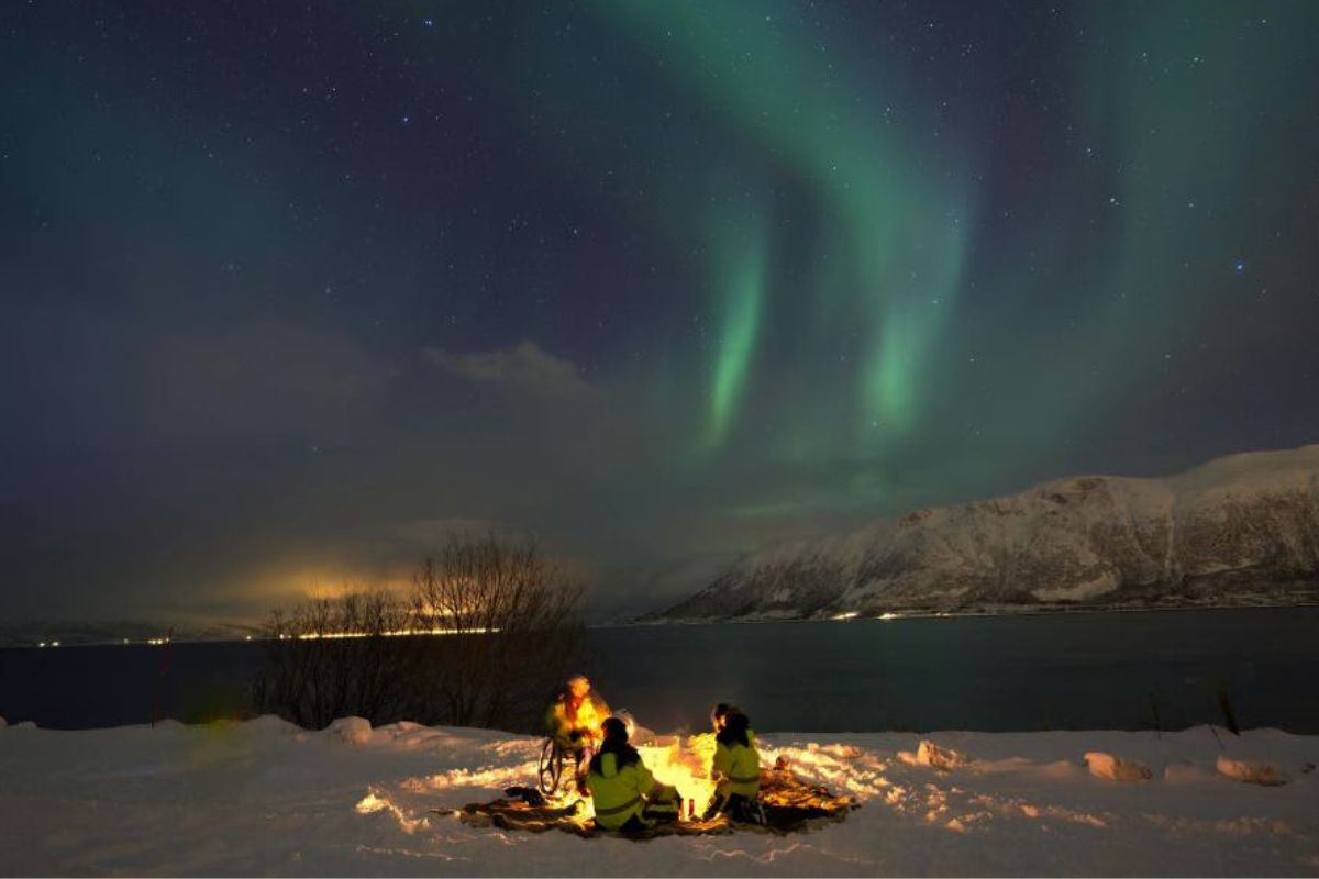 Personas acampando junto a un lago bajo la aurora boreal. (Imagen representativa: Pexels | Luis A. Dumois N.)