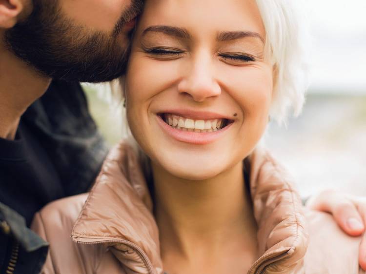 Un hombre le da un beso a su pareja y ella sonríe con felicidad