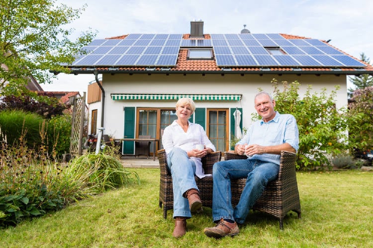 Una pareja sentada frente a una casa con paneles solares en el techo