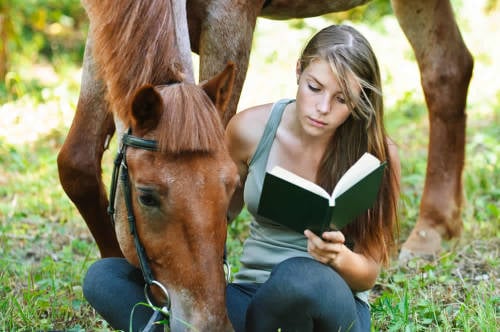 lectura vegana joven lee un libro en la naturaleza mientras acaricia un hermoso caballo