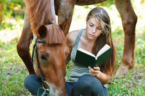 joven lee un libro en la naturaleza mientras acaricia un hermoso caballo