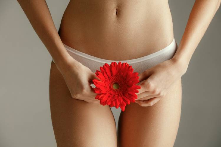 Una mujer sostiene una flor sobre su pelvis