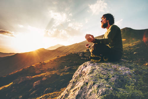hombre medita al amanecer sobre las montañas